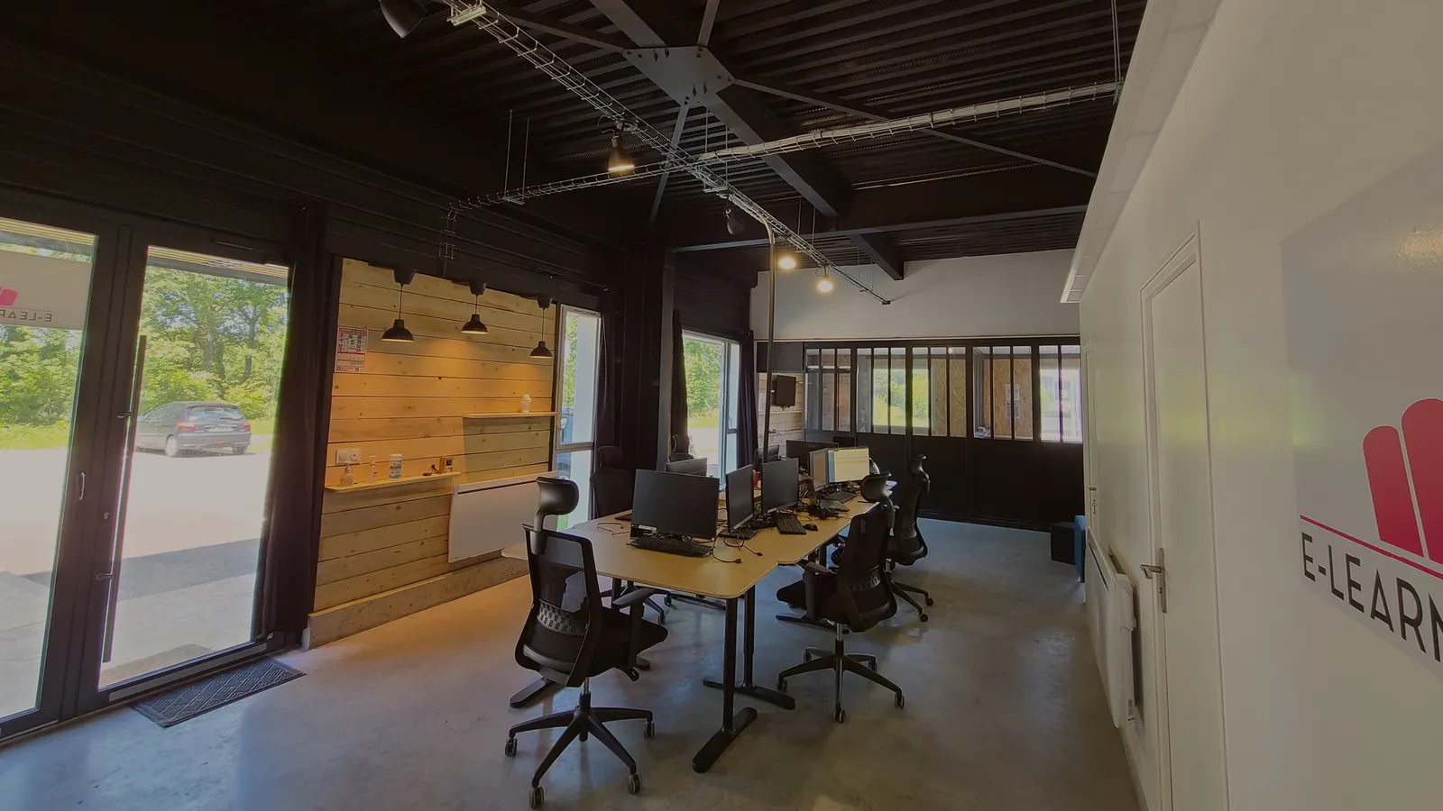 Les bureaux d'E-learning Touch' à Guipavas : grande table de travail, écrans, mur en bois et baies vitrées.