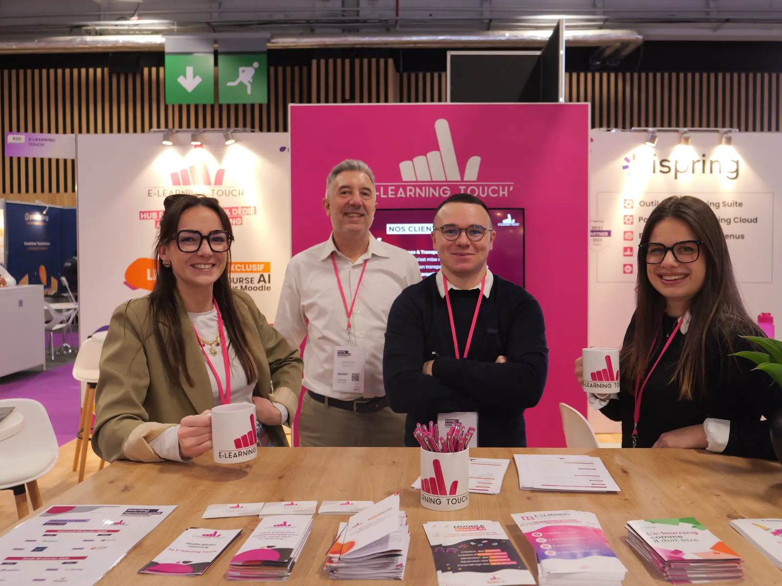 Quatre membres d'E-learning Touch' souriants sur le stand de l'entreprise, lors d'un salon professionnel.
